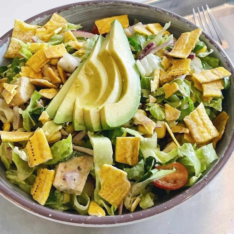 Leaf's fresh salad with lettuce, corn, red onion, tomatoes, tofu, plantain chips, and avocado slices.