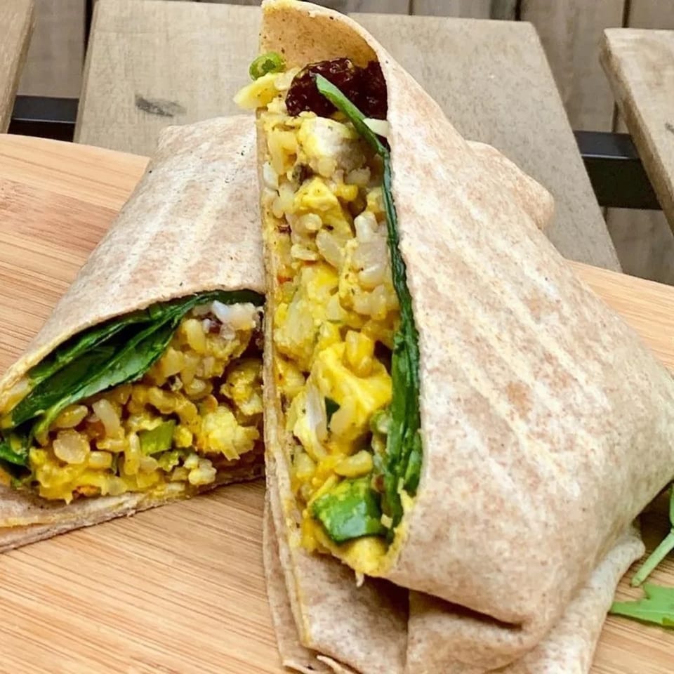 Two halves of a Leaf curry chicken salad wrap with spinach, rice, and avocado on a wooden board.